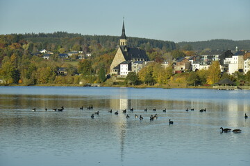 Le lac des Doyards et le village de Vielsalm avec l'&eacute;glise paroissiale Saint Gengoux se refl&eacute;tant dans ses eaux  sous un ciel clair d'automne 