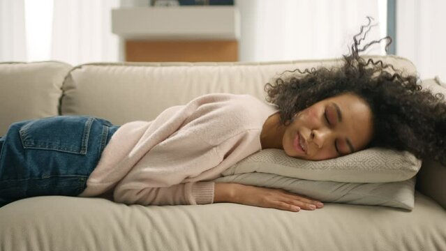 Apathetic bored lady sleeping on couch at home alone. Tired girl lying asleep feeling out of energy motivation, depression concept. Exhausted tired lazy young african american woman falls down on sofa