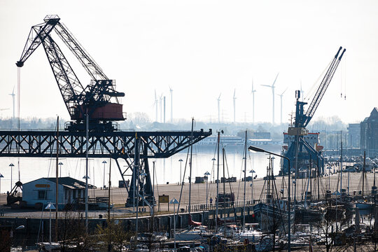 City harbor on the Warnow River in Rostock in Germany. With harbor quay, cranes, boats, wind turbines and warehouses.