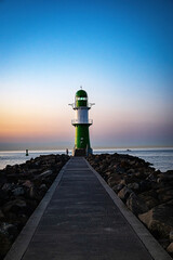 Green lighthouse and stone coast with footpath at the harbor entrance from the Baltic Sea to...