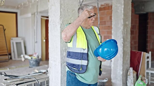 Middle age grey-haired man builder sweating at construction site