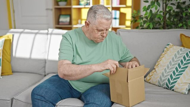 Middle age grey-haired man unpacking cardboard box doing thumbs up gesture at home