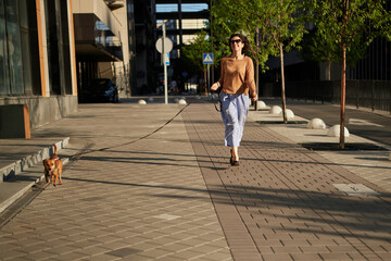 Young pretty female adult with small ginger dog in the bi city walking having fun. City view High quality photo