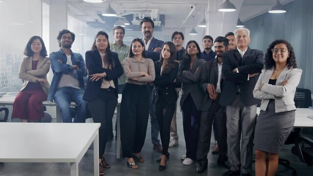 A happy confident large group or team of diverse Asian Indian male and female corporate office executives or colleagues folding hands together and looking at the camera in modern start up business