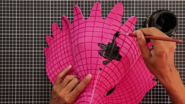 Making crafts. Painting a pink eagle mask, in black. Cutting mat. Brown hands. Arts. 