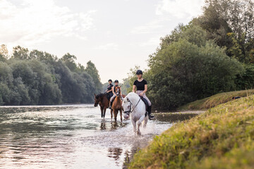 Three girls relaxing in a natural setting, horseback riding across the river during sunset....