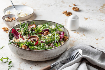 Healthy diet salad with feta cheese, arugula, mushrooms, walnut in ceramic bowl on textured background with text space. Fresh summer lunch or dinner