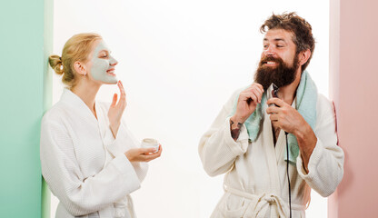 Morning procedures. Couple man and woman doing morning hygiene. Husband with electric shaver, wife with cosmetic facial mask. Morning treatments. Family life together. Couple in bathrobe at bathroom.