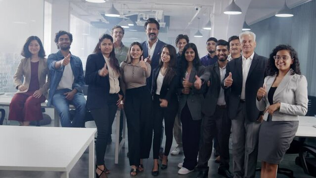 A happy confident Asian Indian group or team of diverse male and female corporate office executive colleagues together showing thumps up sign looking at the camera in a modern start up business