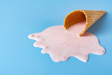 Strawberry ice cream melting and spilling from the waffle cone on blue background. Minimalist summer food concept. Empty copy space