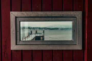 A red wooden window displays a harbor in cold weather on a cloudy day