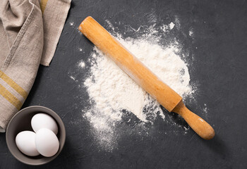 Natural wheat flour is scattered on a dark background with eggs and napkin. The concept of an organic product for home baking.