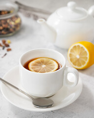 Tea with lemon in a white cup on a light background with  a teapot close up. The concept of a healthy and tasty breakfast for immunity