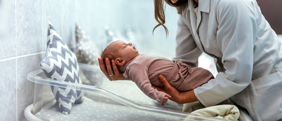White female doctor or nurse is holding small infant. Newborn baby in hospital at neonatal...