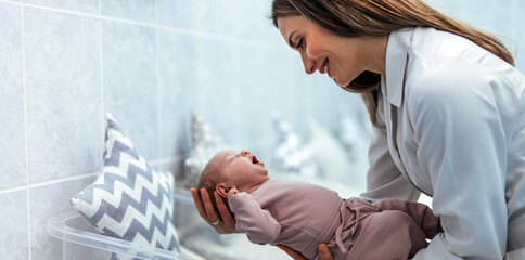 Female nurse with premature born baby in intensive care unit holding infant in her hands. Pediatrician nurse taking care of newborn baby at hospital ward. She is holding baby while mother is resting.