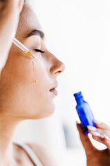 Attractive girl drops essential oil on facial skin close-up. Young woman is applying moisturizing serum on her face.