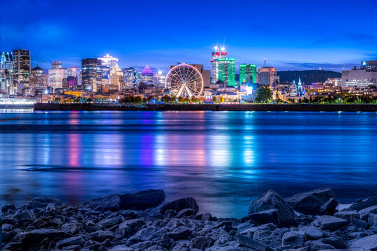 Acenic view of downtown Montreal from the Saint Lawrence River at night, with the city lights reflecting in the river.