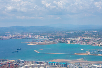 Fototapeta na wymiar Gibraltar, Aerial view on buildings, city and coast of sea. Crystal clear blue water against mountains