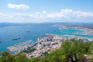 Fototapeta na wymiar Gibraltar, Aerial view on buildings, city and coast of sea. Crystal clear blue water against mountains
