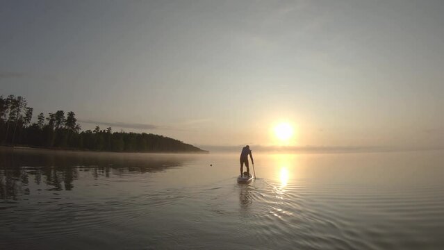 Man paddling on stand up paddle board at dawn. SUP boarding