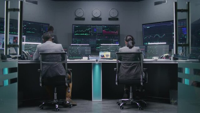 Multi ethnic team of financial analysts work on computer with displayed real-time stocks in modern office. Colleagues analyze exchange market charts on big screens. Investment and trading. Dolly shot.