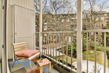 a balcony with some chairs and trees in the back yard, as seen from an open window on a sunny day