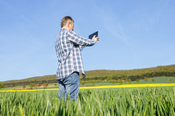 A man with a digital tablet in his hands in a rye field. The farmer inspects the crop and writes down the readings on the tablet. Technologies in agriculture.