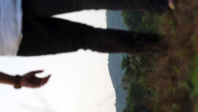 A man wearing white shirt walking towards a hill through a meadow