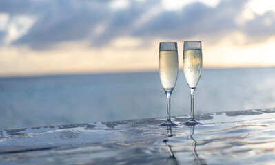 Two glasses of champagne on the side of the infinity pool against the backdrop of a sunset in the Maldives