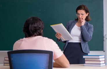 Old female teacher and male student in the classroom