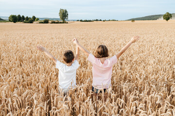 Happy boy and girl stand in a field with ears of rye and hold hands. Happy and free children in the...