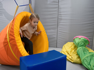 Child girl in roller tonnel during sensory integration session. child with physiotherapist in...