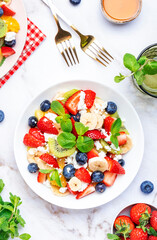 Fresh fruit and berry salad with cottage cheese, strawberries, blueberries, kiwis, oranges and mint leaves with honey dressing, marble table background, top view