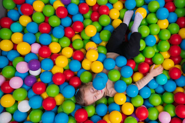 Fototapeta na wymiar Cute little girl playing on multi coloured plastic balls in big dry paddling pool in playing centre. Having fun in playroom