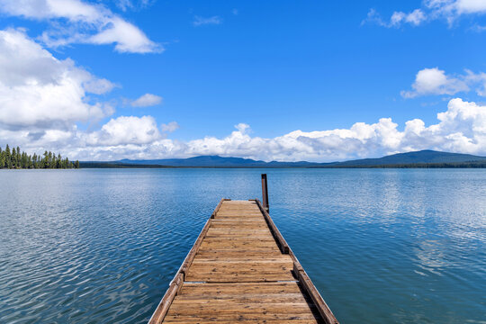 Boat Ramp at Blue Mountain Lake - A long wooden boat ramp extending onto a blue mountain lake under Spring blue sky and white clouds. Crane Prairie Reservoir, Bend, Oregon, USA.