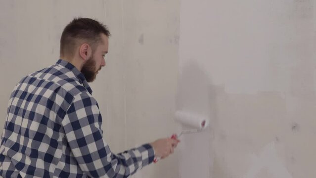 Handsome man painting wall with roller brush. Renovation house. Redesign and improvement new home 