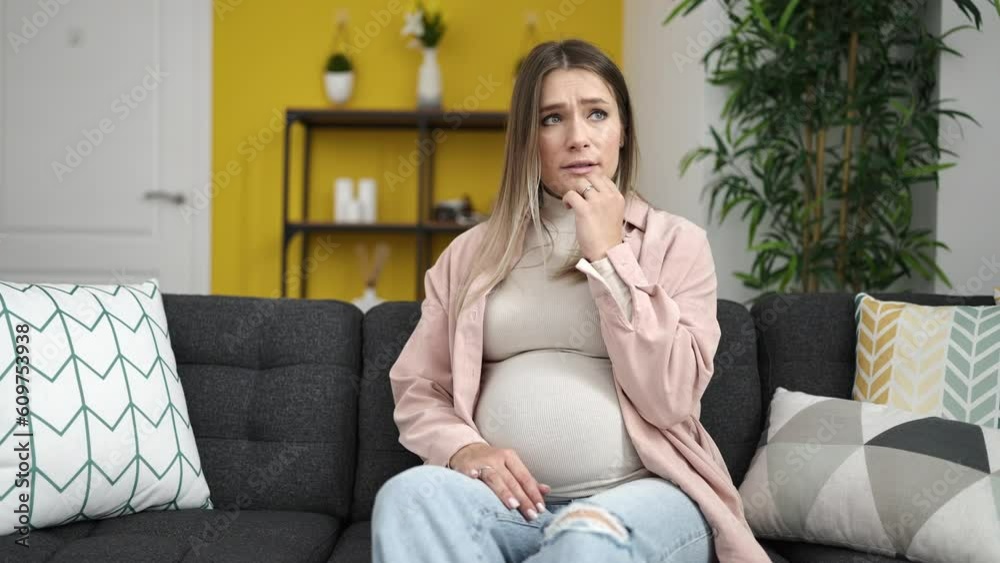 Wall mural Young pregnant woman touching belly with worried expression at home