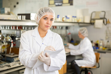 Female scientist engaged in research in chemical laboratory noting results in test chart