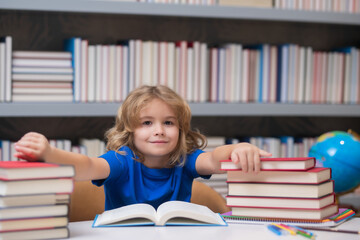 Little student read book. School boy doing homework on desk in school library. Pupil child studying homework literature near pile of books. Kid reads a book with shelves stacks of books.