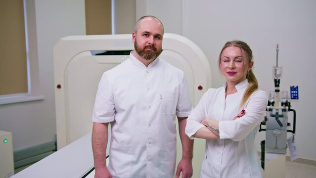 smiling and satisfied doctors in uniform posing near magnetic resonance imaging machine concept of professions and medicine