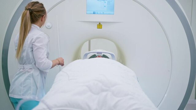 A professional radiologist in a medical clinic monitors a patient undergoing a magnetic resonance imaging procedure