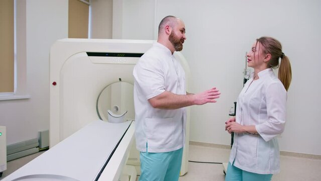 smiling and satisfied doctors in uniform discussing the conducted study near magnetic resonance imaging concept of professions and medicine