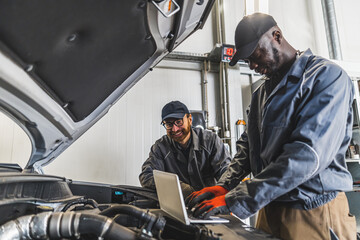 Two men mechanics completing car engine diagnostics with laptop in a repair shop. High quality photo