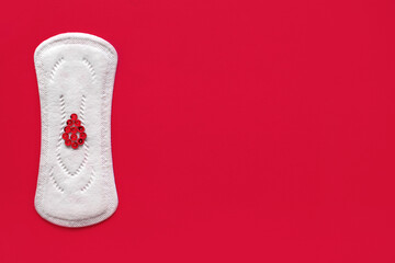 Menstrual pad with red sequins in the form of a drop of blood on a red background. Free space for text. The concept of menstruation in women. Tool to stop bleeding during the menstrual cycle