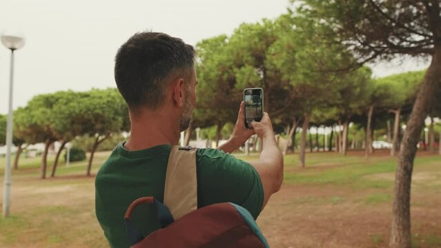 Middle aged man tourist taking photo while standing in city park