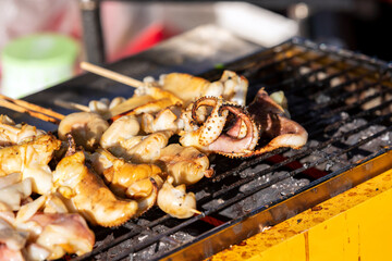Large squid skewers are grilled on a hot stove. in the evening The sun shines from the side.It is a delicious street food that is very popular in Thailand. Selective focus.
