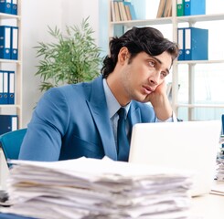 Young handsome male employee with too much work in the office