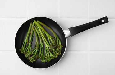 Frying pan with tasty cooked broccolini on white tiled table, top view