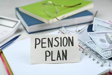 Naklejka premium Card with phrase Pension Plan, notebook and dollar banknotes on office table, closeup
