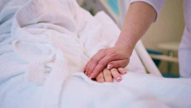 A doctor's hands holding a patient's hands as a sign of care and support close-up in a hospital room